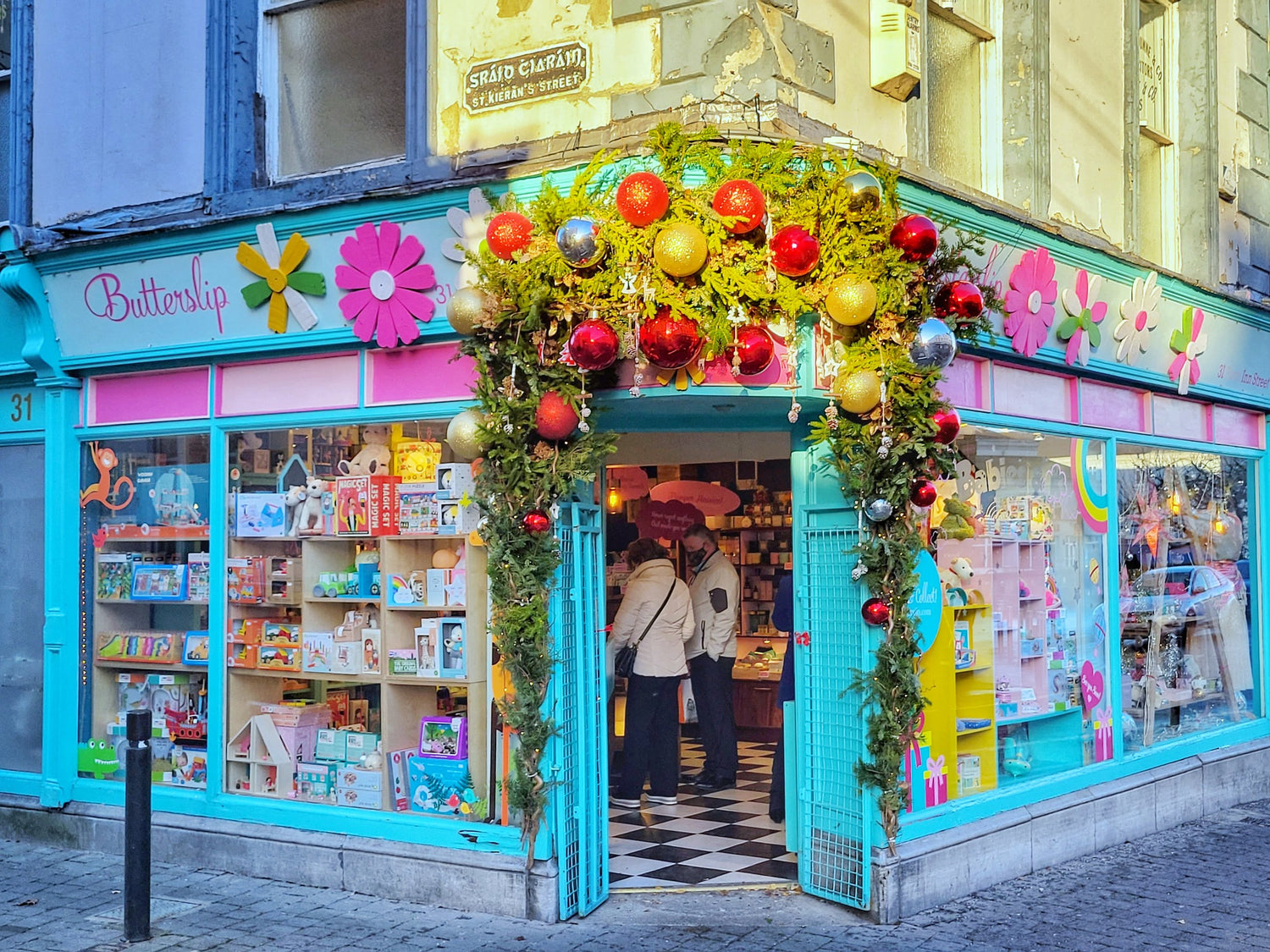 Shopfront with a tall Christmas wreath of greenery and red and gold baubles, with bright window decorations
