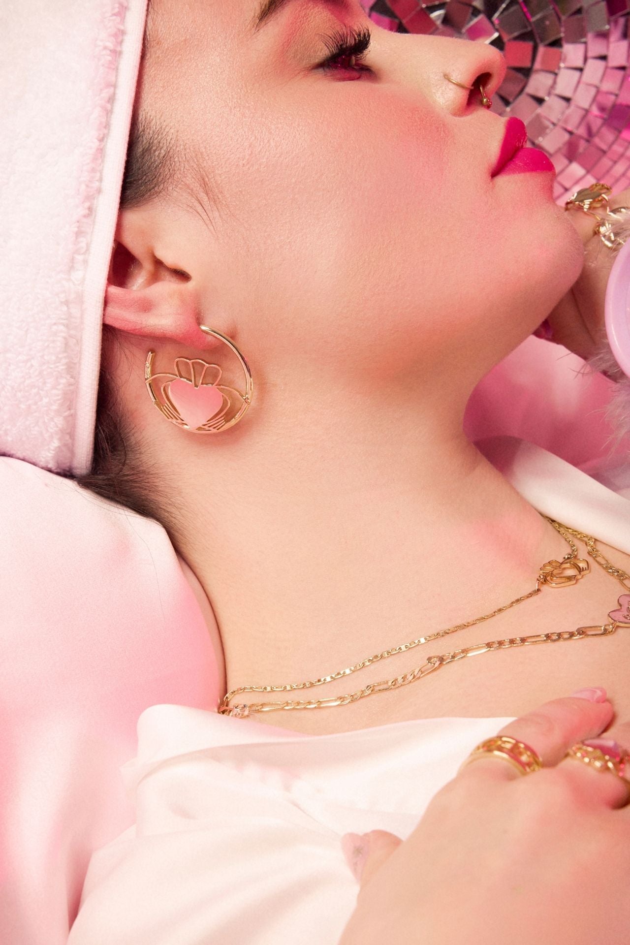 Close-up of a person wearing gold earrings and necklaces with a pink background