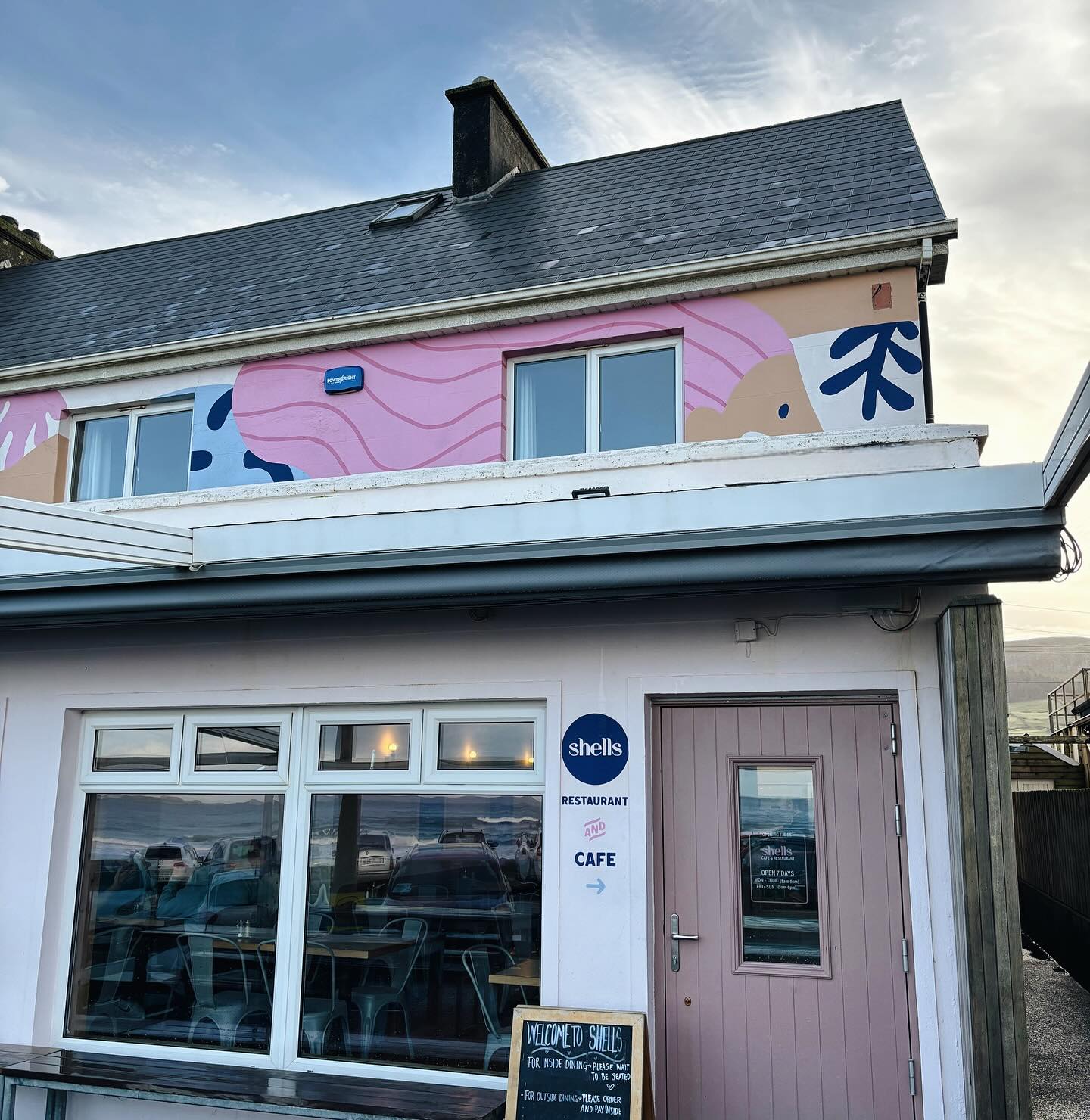 Cafe building with dark tiled roof, mural windows and sign reading shells restaurant and cafe