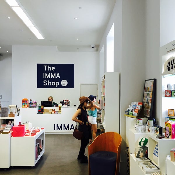 Retail shop interior with The IMMA Shop sign, shelves of toys and books, and people walking past