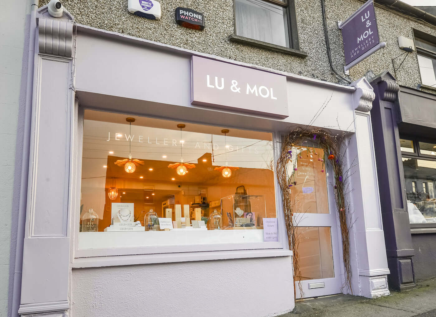 Shopfront with LU and MOL sign, phone watches notice, and jewellery display window with warm lights