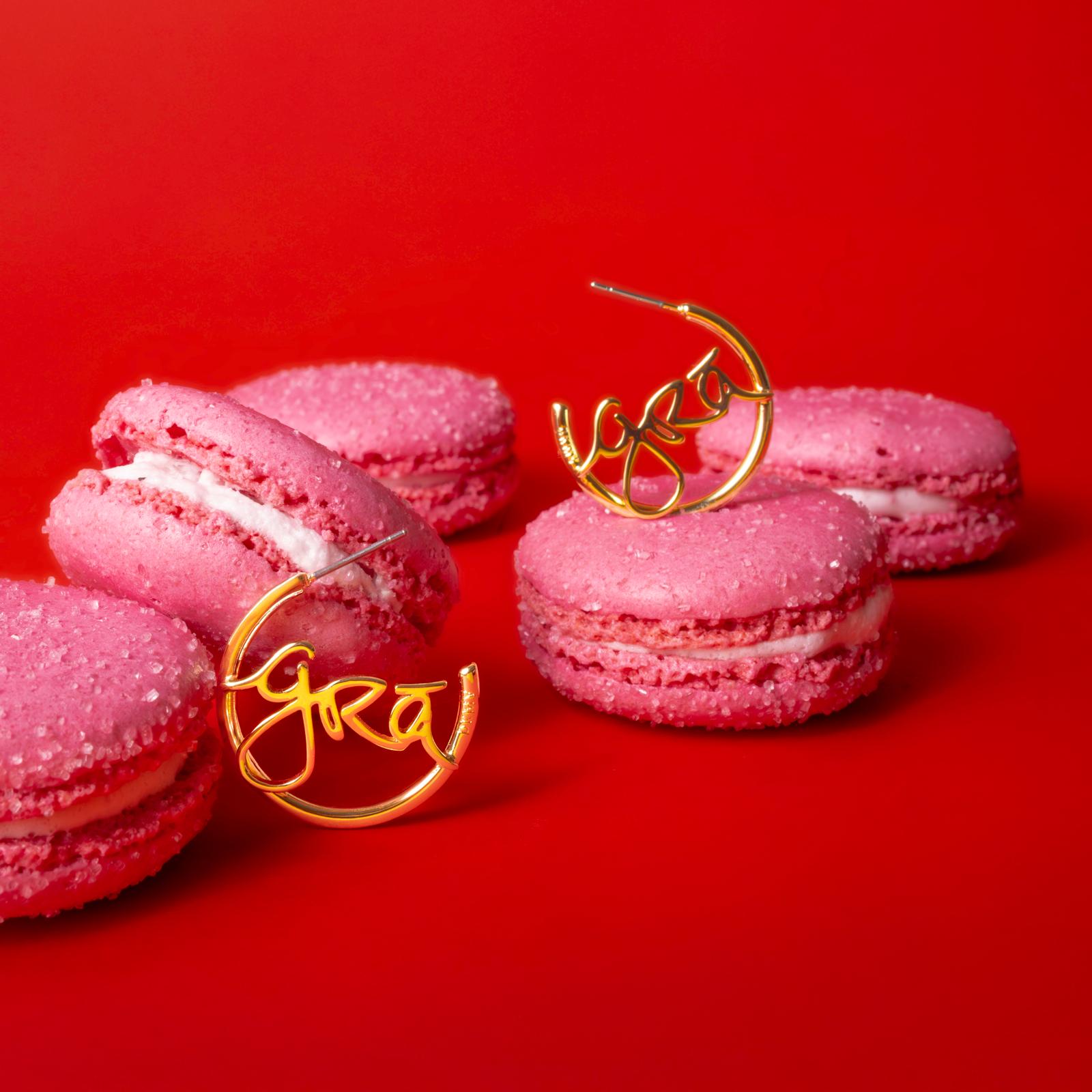 Pink macarons with white filling on a red background, with gold cursive decoration in the centre