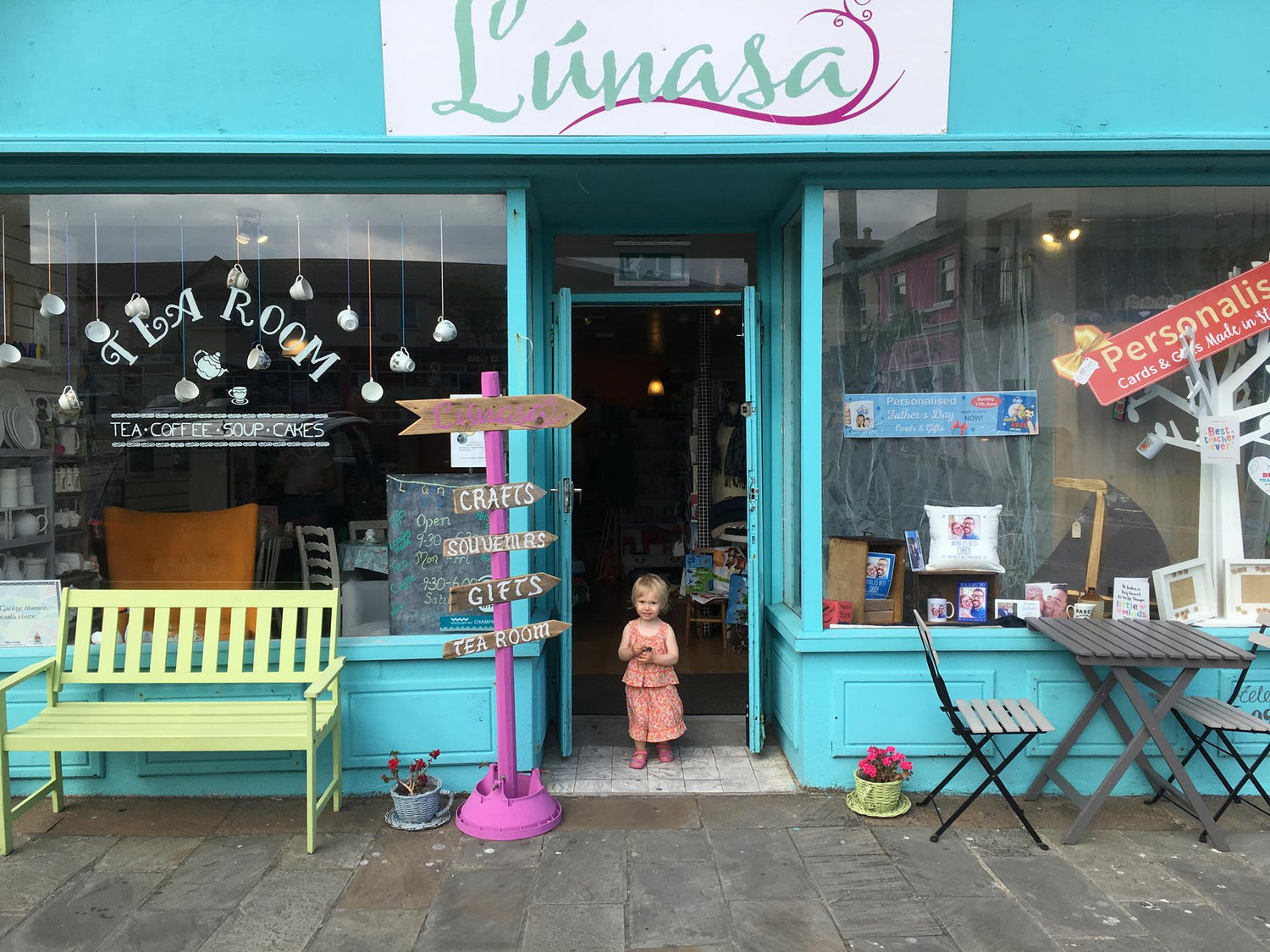 Tea room doorway with teal frontage, hanging teapots in the window, and a child standing outside