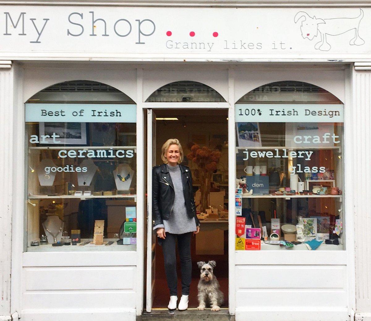 Shop entrance with a woman and small dog standing in front of a window display of Irish craft